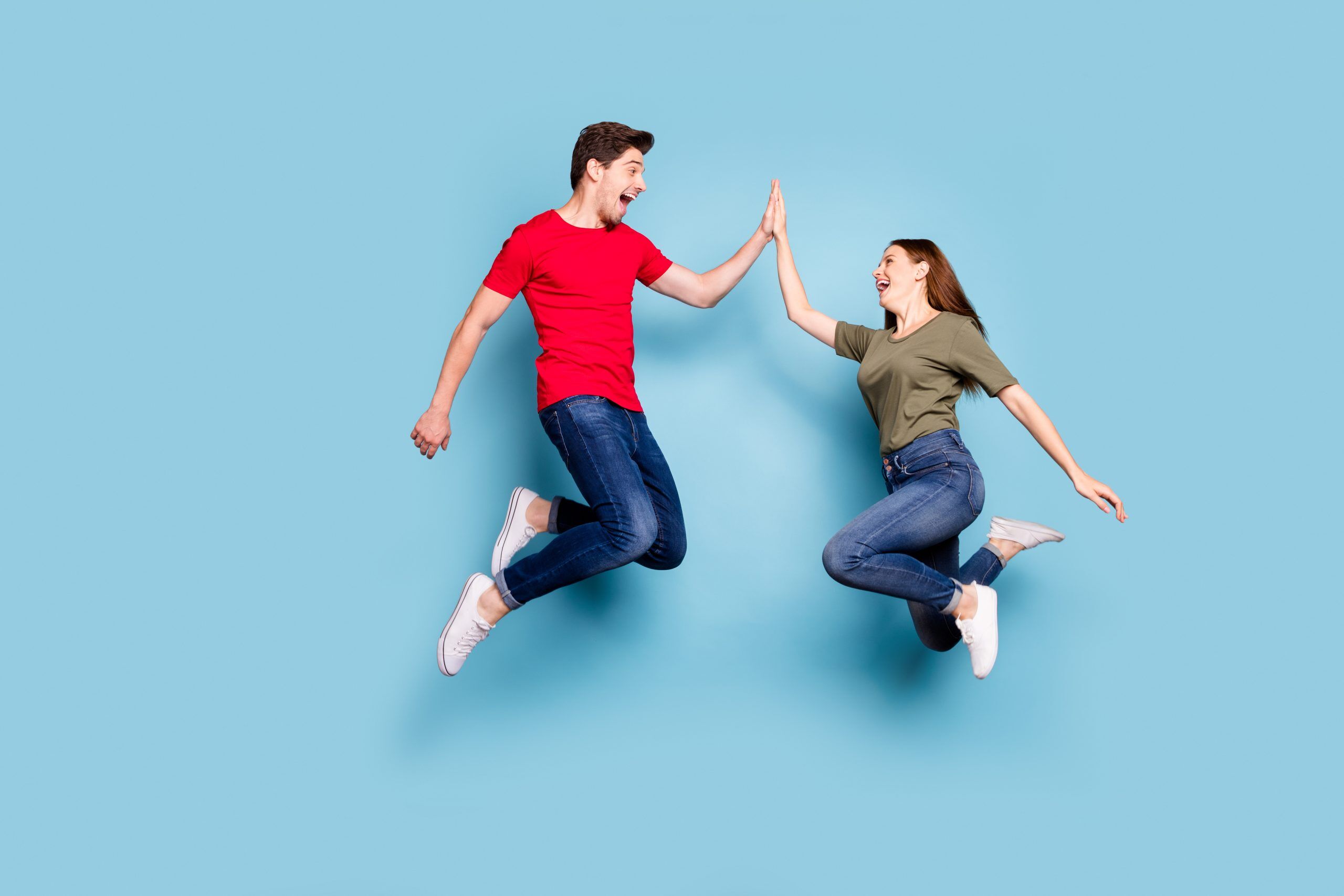 Great job. Full length profile side photo of cheerful two romantic people jump, give highfive celebrate victory wear modern t-shirt denim jeans sneakers isolated blue color background