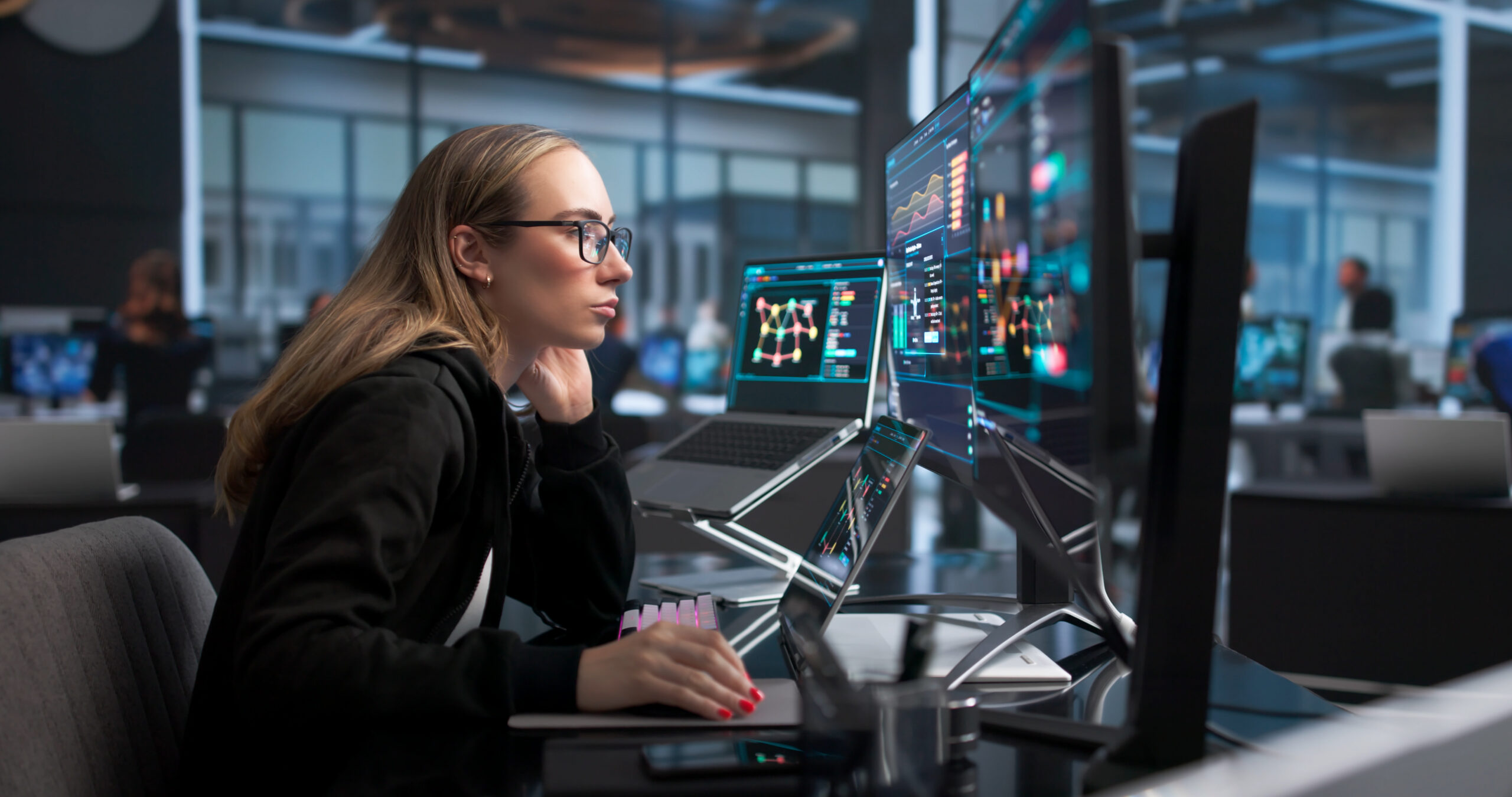 Woman Monitors Network Security Alerts On Laptop In Busy Data Center.
